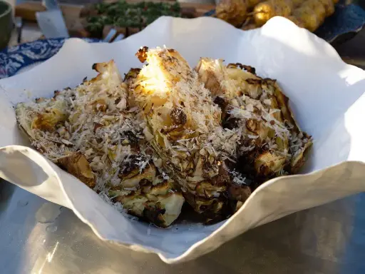 Grillad spetskål serverad i en vit skål, toppad med riven ost och hackade nötter. En härlig rätt för grillkvällen.