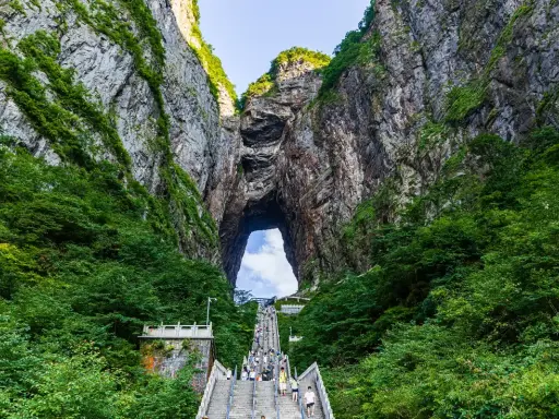 Eine lange Treppe führt durch eine Schlucht mit üppiger Vegetation hinauf zu einem riesigen Felsentor, den "Stairs to Heaven" in China.