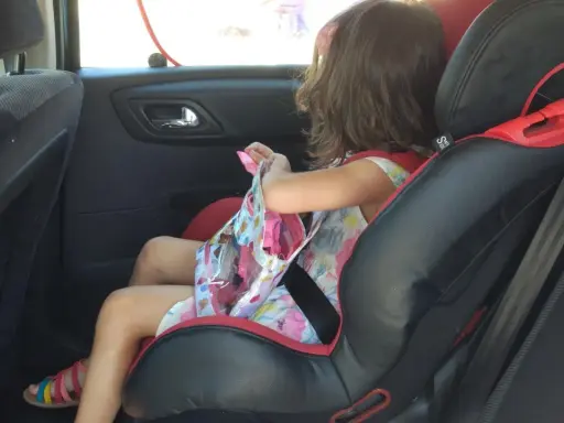 Niña en silla de coche, lista para el viaje. Aún no es el momento cuando puede ir un niño sin silla en el coche.
