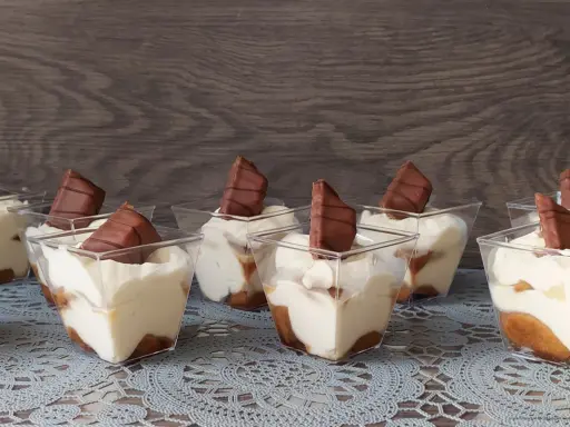 Słodkie deserki w pucharkach, przypominające tort Kinder Bueno, z kremem i kawałkami czekolady.