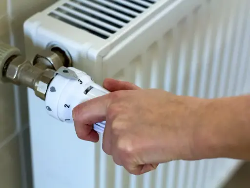 Dłoń reguluje termostat grzejnika. Kiedy zaczyna się sezon grzewczy? Zazwyczaj od października do kwietnia.