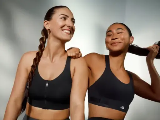 Two women in black sports bras, one with a braid, the other playing with her hair.