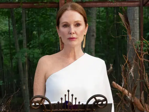 Julianne Moore i den vita klänningen i "Sirens"-serien, med en bakgrund av skog och dekorationer av fjädrar och kvistar.