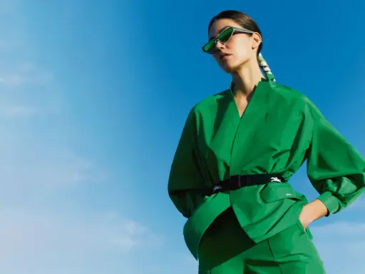 Une femme en tenue verte éclatante, lunettes de soleil futuristes, pose sous un ciel bleu. Un **cahier de tendance** inspirant.