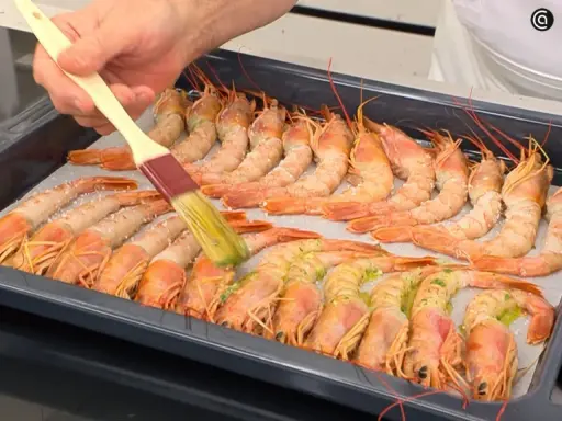 Un pincel baña con aceite y hierbas unos gambones al horno listos para cocinar.