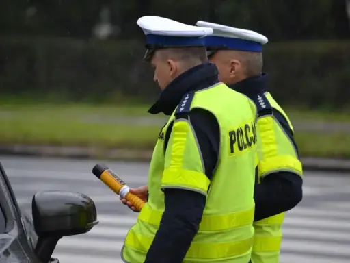 Policjant w kamizelce odblaskowej trzyma alkomat. Czy policja może badać alkomatem w domu? To pytanie często zadawane przez kierowców.