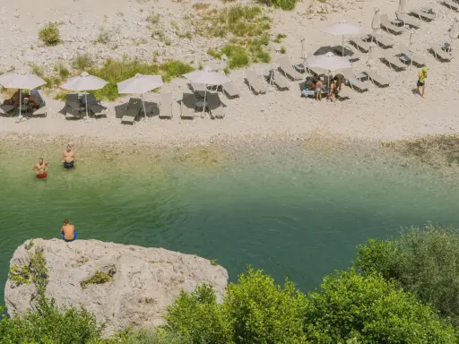 Wczasy w Albanii: ludzie odpoczywają na plaży nad krystalicznie czystą wodą, niektórzy kąpią się, inni relaksują pod parasolami.