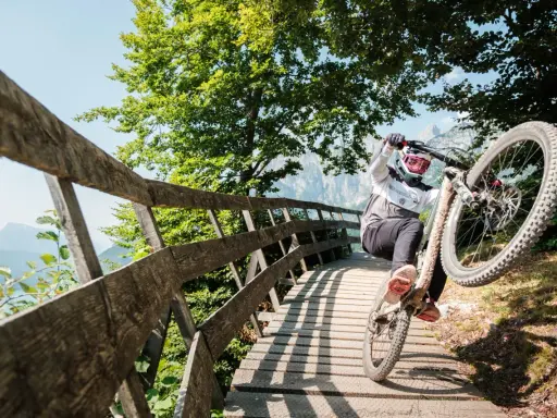 Ciclista in azione durante il giro del lago di Molveno in bici, su un ponte di legno tra alberi verdi e montagne.