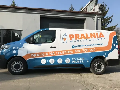 Biało-niebieski van z pomarańczowymi elementami to reklama tranzytowa dla pralni. Na boku widnieje napis "PRALNIA WARSZOWIANKA" i numer telefonu.