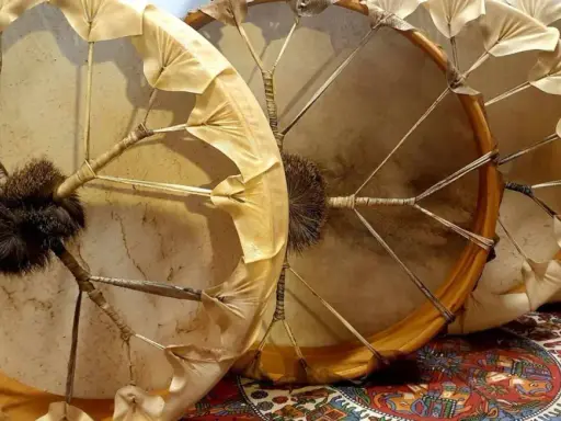 Trois tambours chamaniques, un instrument traditionnel aux peaux tendues et ornées de franges, prêts pour une cérémonie.