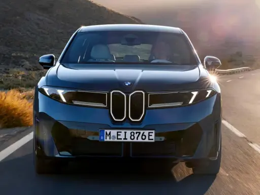 Der BMW iX4 fährt auf einer kurvigen Straße durch eine bergige Landschaft im goldenen Licht der Abendsonne.