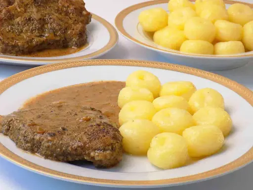 Pyszna karkówka w sosie, podana z kluskami śląskimi. Danie wygląda apetycznie i zachęca do spróbowania.