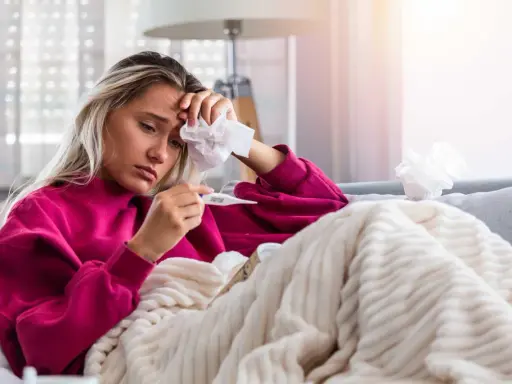 Donna malata con termometro e fazzoletto, preoccupata per il suo stato, forse **immunodepresso significato** da approfondire.
