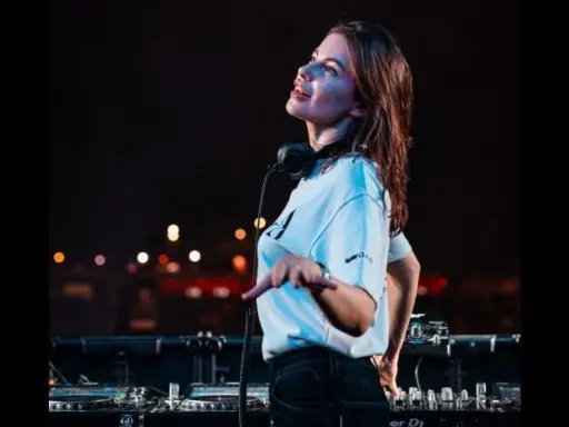 Anfisa Letyago, giovane DJ, con cuffie al collo, mixa musica dal vivo. La sua età è un mistero, ma la sua passione è evidente.
