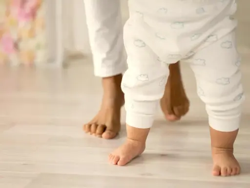 Un bebé da sus primeros pasos, guiado por un adulto. Un momento tierno que ilustra cómo educar a un bebé: con amor y apoyo.