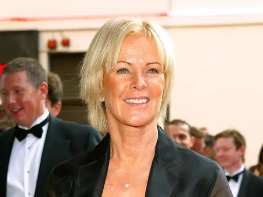 Anni-Frid Lyngstad, känd som Frida, ler med en hjärtformad halsband. Hon är klädd i en svart kavaj.