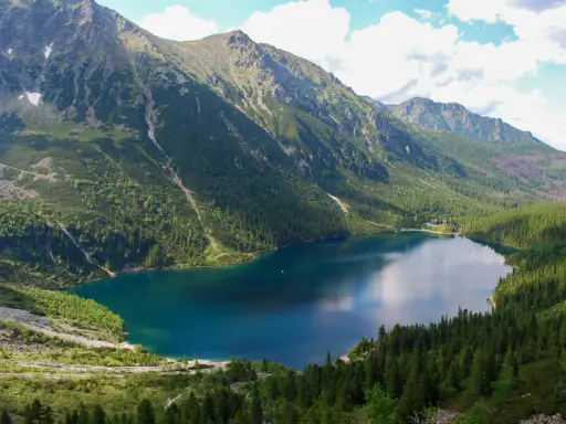 Górskie jezioro otoczone lasem, z wodospadem spływającym po zboczu. Widok przypomina, jak powstało Morskie Oko.