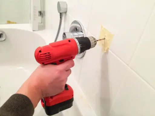 Main tenant perce le carrelage de la salle de bain pour installer un accessoire.