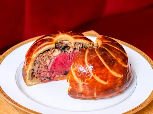 Un pâté en croûte aux couches généreuses, un délice d'antan origine, sur une assiette blanche bordée d'or.