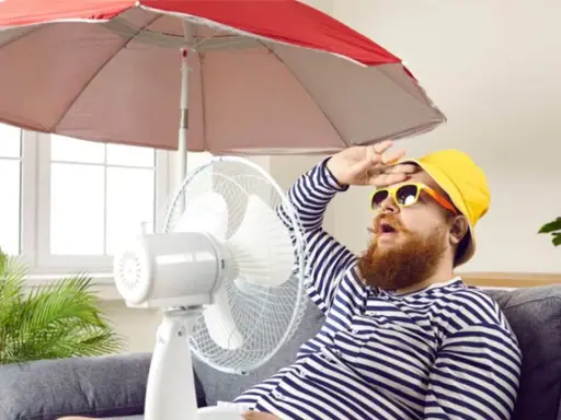 Un homme transpire sous un parasol, ventilateur et plante pour comment rafraichir sa maison. Il a chaud.