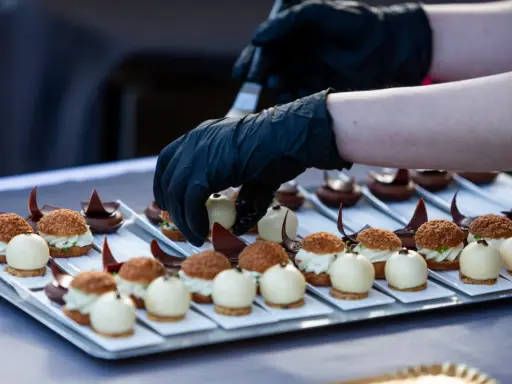 Mains de chef en gants noirs disposant des bouchées, une spécialité culinaire de Metz, sur un plateau.