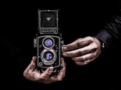 Dwie ręce trzymają aparat Rolleiflex, jedna reguluje ostrość. Sztuka fotografii, zasada złotego środka w kadrze.