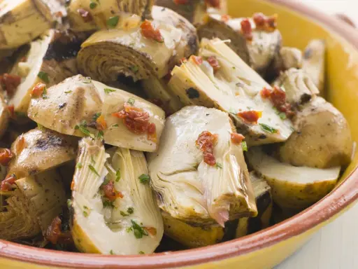Ein köstlicher Artischockensalat mit getrockneten Tomaten und Kräutern in einer gelben Schüssel.
