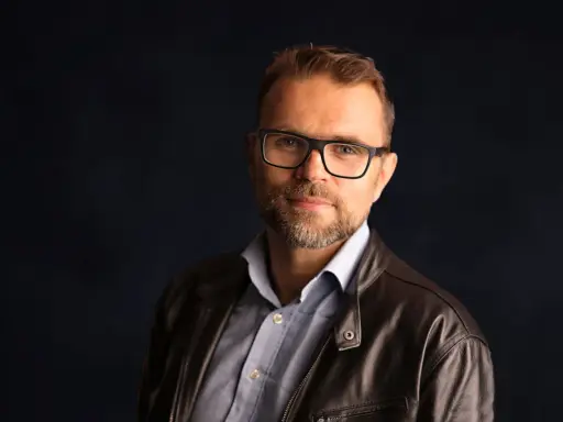 Jacek Bartosiak, autor książek, w okularach i skórzanej kurtce, patrzy w obiektyw.