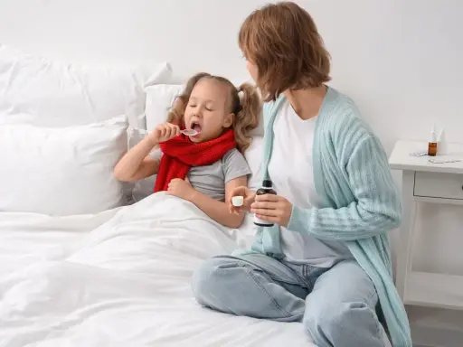 Bambina malata a letto prende sciroppo, mentre la mamma tiene il flacone. Forse per febbre o tosse, un mix di brufen e tachipirina insieme per farla stare meglio.