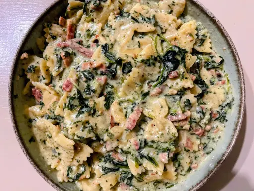 Pyszny makaron farfalle w kremowym sosie ze szpinakiem i kawałkami boczku.