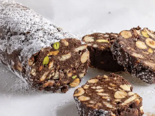 Salame di cioccolato senza uova ricetta della nonna, con biscotti, nocciole e pistacchi, spolverato di zucchero a velo.