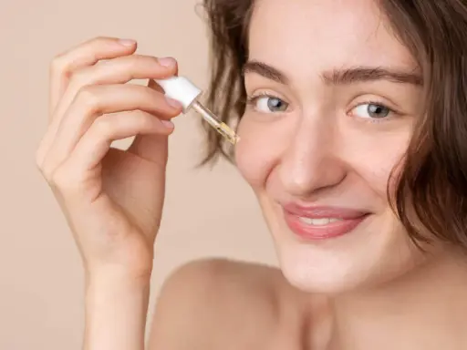 Une femme souriante applique une goutte de sérum à la vitamine C sur son visage. C'est le moment idéal pour utiliser la vitamine C sur le visage pour une peau éclatante.