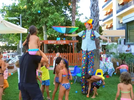Hotel con biberoneria: animazione al Baby Club con un clown che intrattiene i bambini con palline colorate e un ombrello arcobaleno.