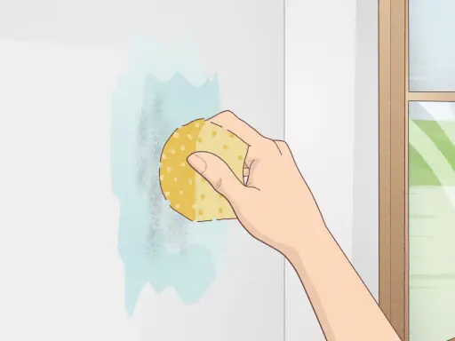 Mano limpiando una mancha en una pared blanca con una esponja. Aprende como limpiar paredes blancas fácilmente.