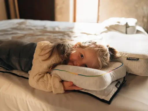 Ein kleines Mädchen kuschelt sich auf einem Bett an ein Kissen. Die Schlafphasen von Kindern sind wichtig für ihre Entwicklung.
