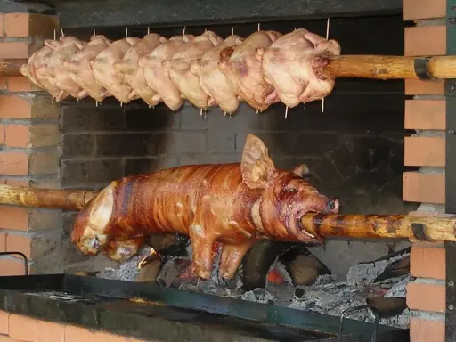 Ein Spanferkel grillen über offenem Feuer. Darüber hängen mehrere Hähnchen am Spieß.