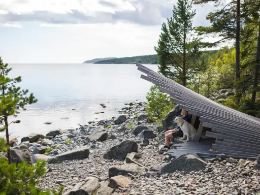 En man och hans hund njuter av en lugn semester vid vattnet, omgivna av stenar och träd.