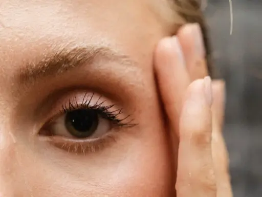 Un œil attentif, cils longs, et le début du repousse sourcils après chimio. Une main effleure le visage.