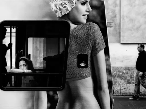 Un'istantanea di vita urbana che ricorda i fotografi di moda, con una ragazza che guarda fuori da un finestrino e un uomo che cammina sullo sfondo.