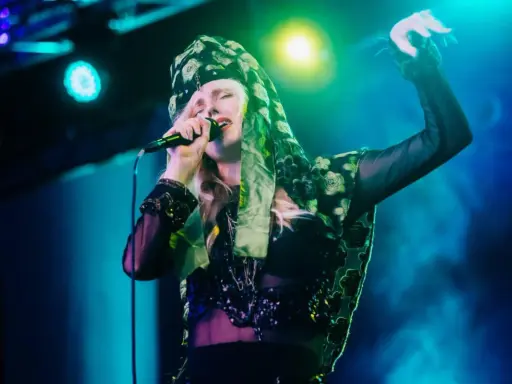 Amanda Jenssen konsert. Hon sjunger med en mikrofon i handen, klädd i en blommig scarf och en glittrig topp.
