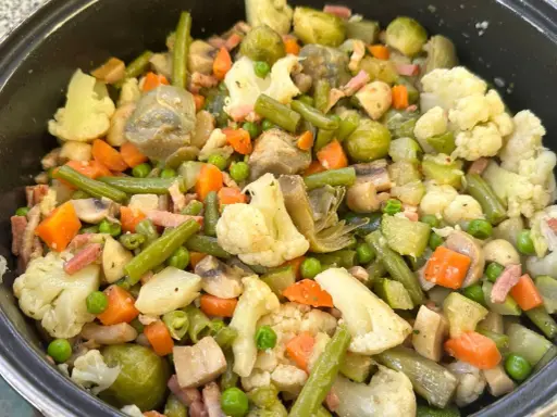 Un plato abundante de menestra de verduras, con brócoli, zanahoria, judías verdes, guisantes y trozos de tocino.