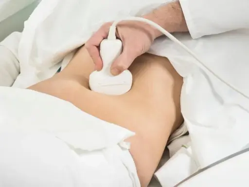 Lekarz wykonuje badanie usg prostaty. Pacjent leży pod białym obrusem, a sonda aparatu USG jest przykładana do brzucha.