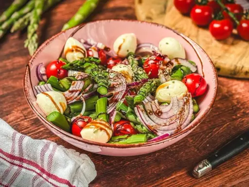 Frischer Spargelsalat mit Ei, Tomaten, roten Zwiebeln und Mozzarella-Kugeln, beträufelt mit Balsamico-Dressing.