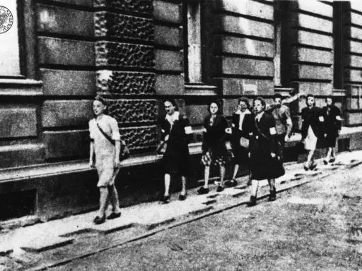 Kobiety w powstaniu warszawskim, idące ulicą. Na ramionach mają opaski.