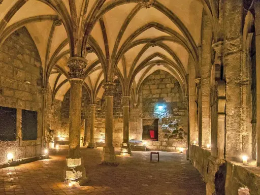 Gewölbte Gänge in einem **kloster mittelalter**. Säulen tragen das steinerne Dach, Kerzenlicht erhellt den Boden.