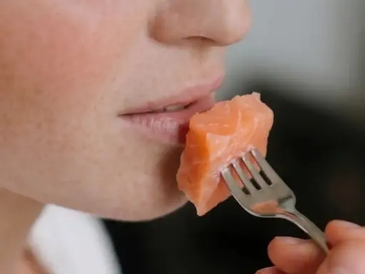 Une personne mange un morceau de saumon à la fourchette. Un aperçu de son visage, idéal pour un avis sur le régime Natman.