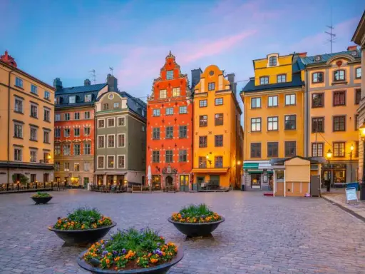 Färgglada hus på ett kullerstens torg i Gamla Stan, Stockholm, med blomkrukor i förgrunden.