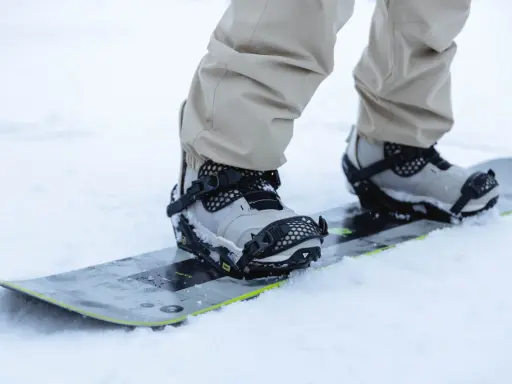 Snowboarder w beżowych spodniach zapina wiązania snowboardowe szybkie zapinanie. Gotowy na jazdę po śniegu.