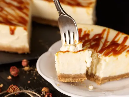 Une fourchette prélève un morceau crémeux de cheesecake, révélant le fromage frais onctueux sous un filet de caramel.