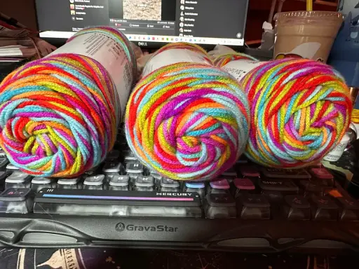 Three balls of brightly colored, variegated yarn sit on a keyboard.